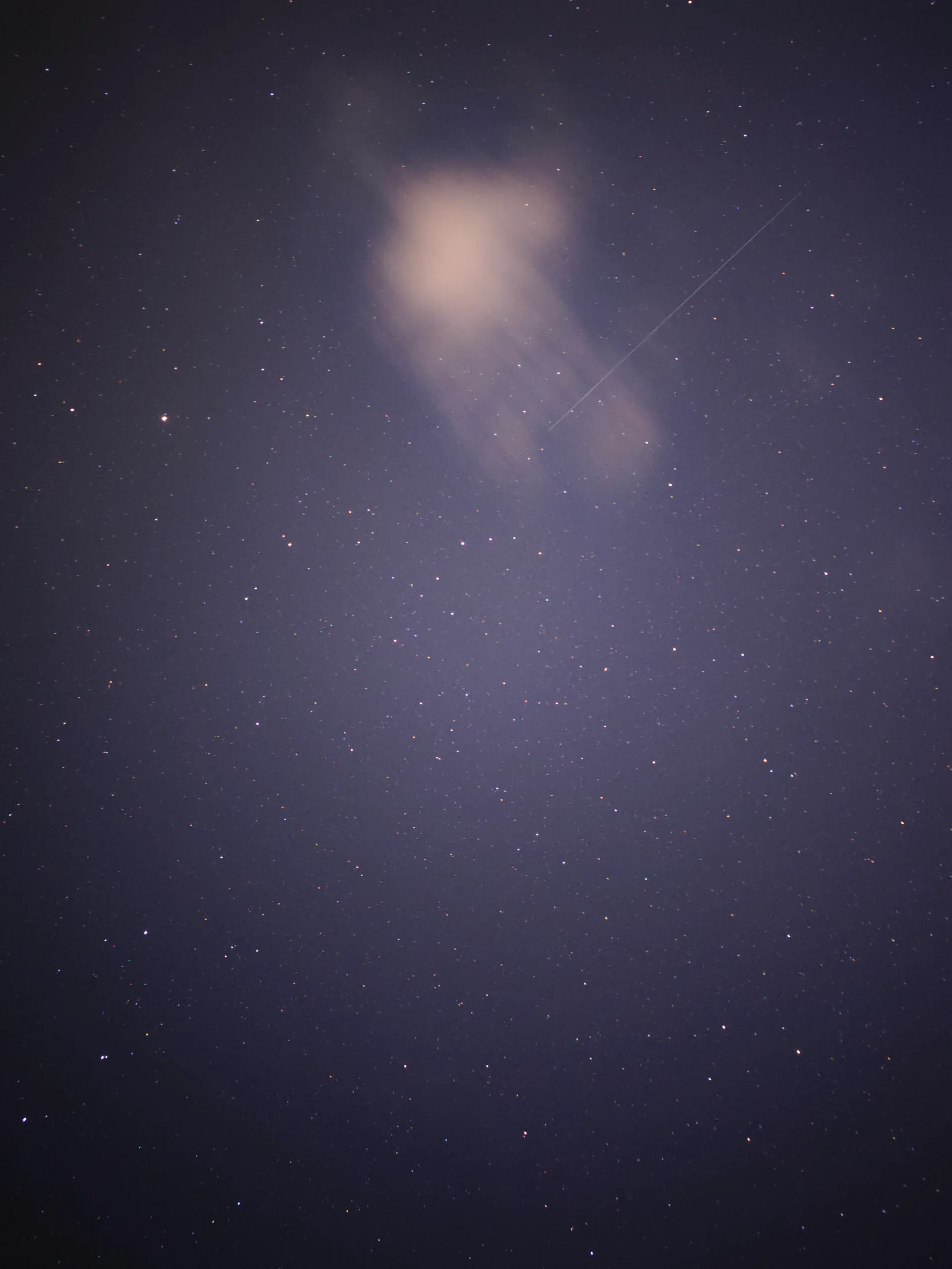 薄云遮住明亮的月亮，周围深蓝夜空布满星点与一道细长光迹